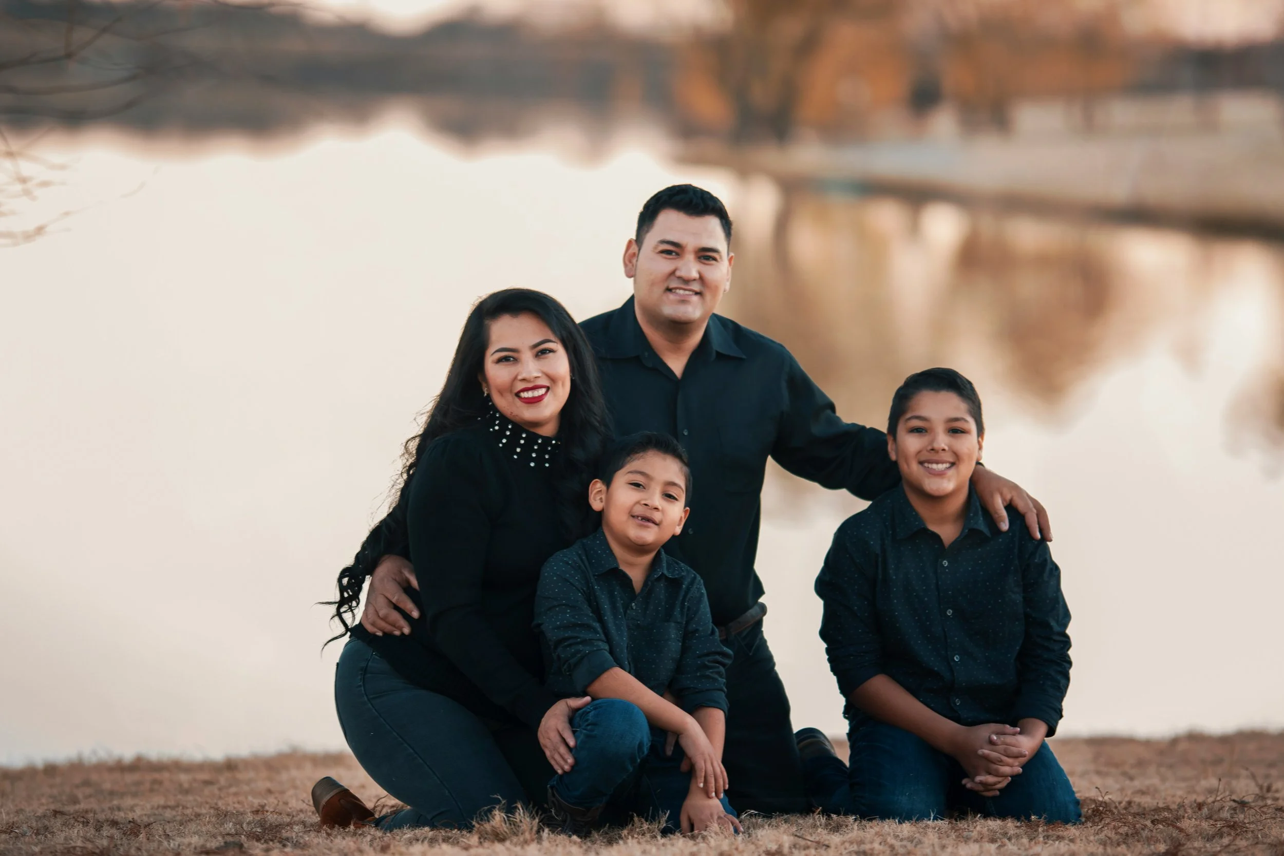 Family of four posing together by a lake, with two adults and two children smiling at the camera.