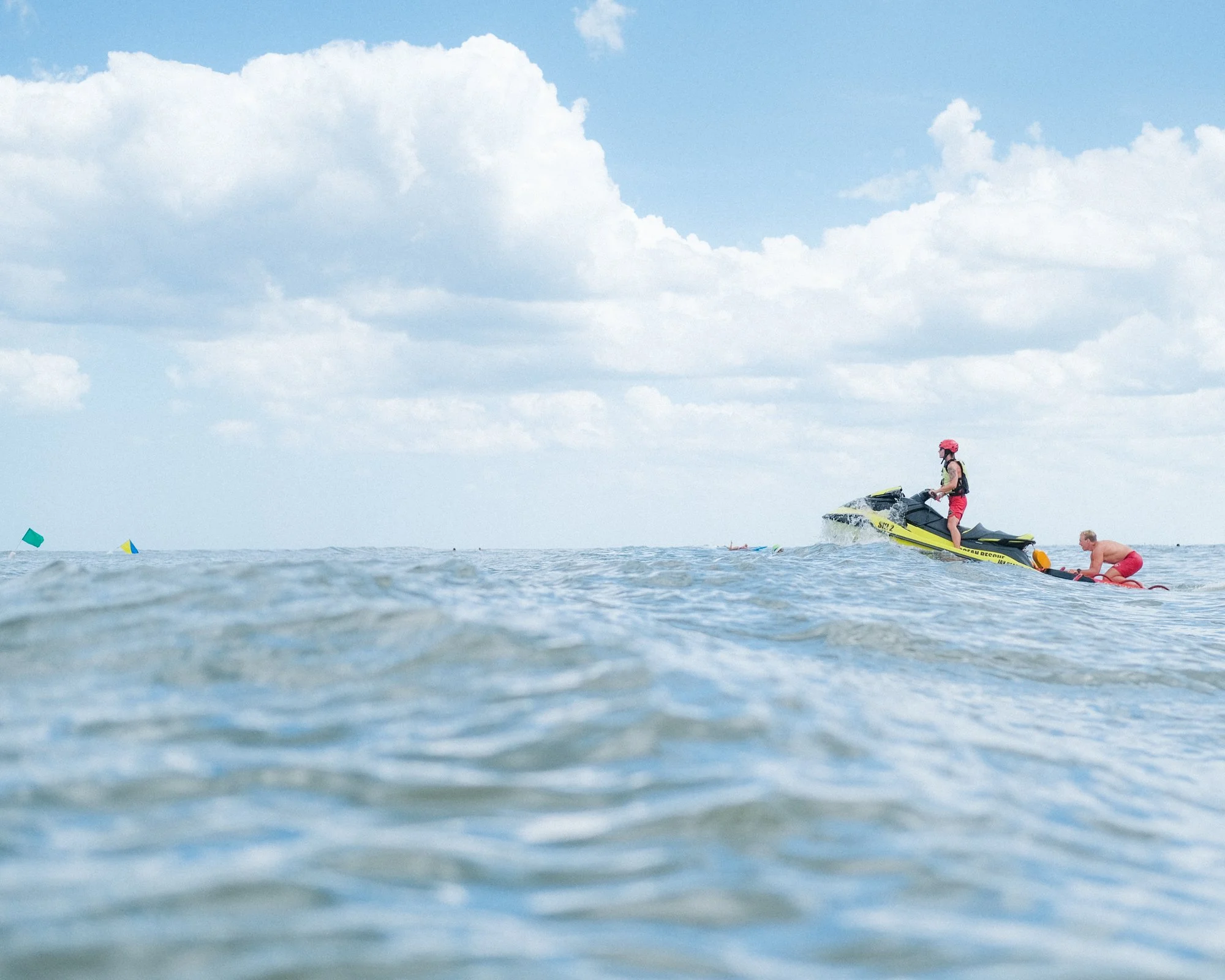 Person riding a jet ski on the water, wearing a helmet and life vest, with a cloudy sky above.