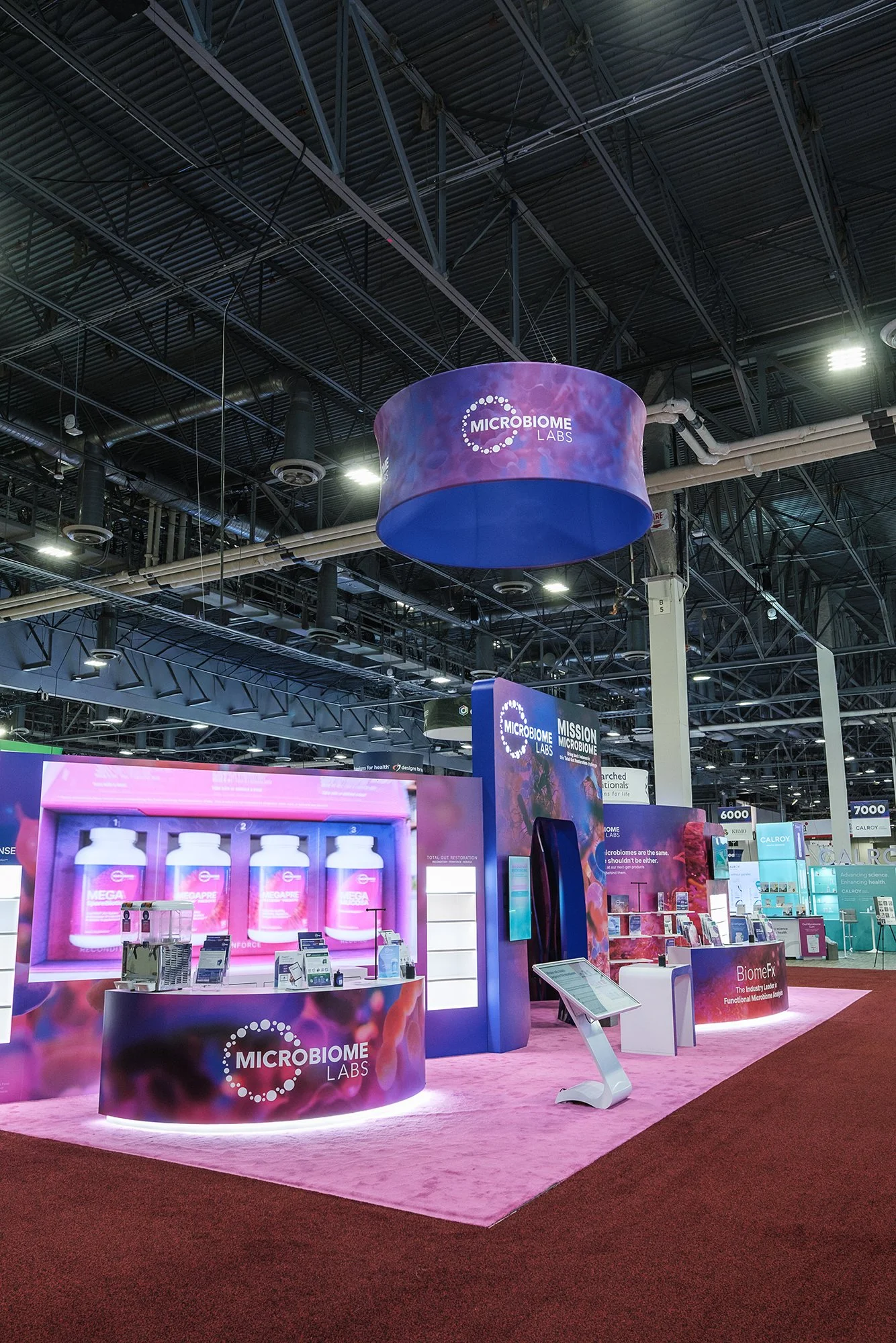 Exhibit booth for Microbiome Labs at a trade show, featuring displays with products and informational signage, with a purple and pink color theme.