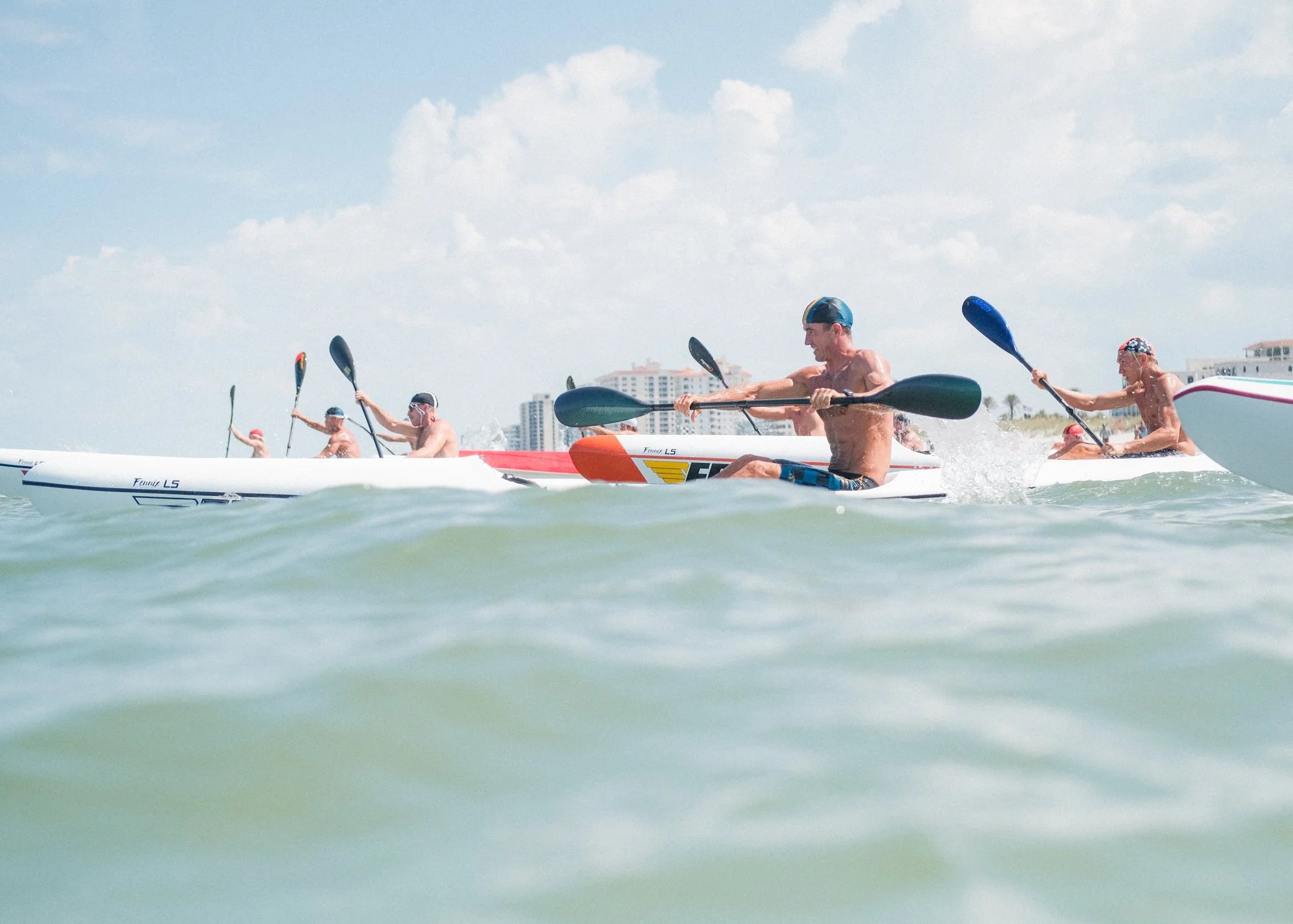 A group of people kayaking in the ocean on a bright sunny day with a city skyline in the background.