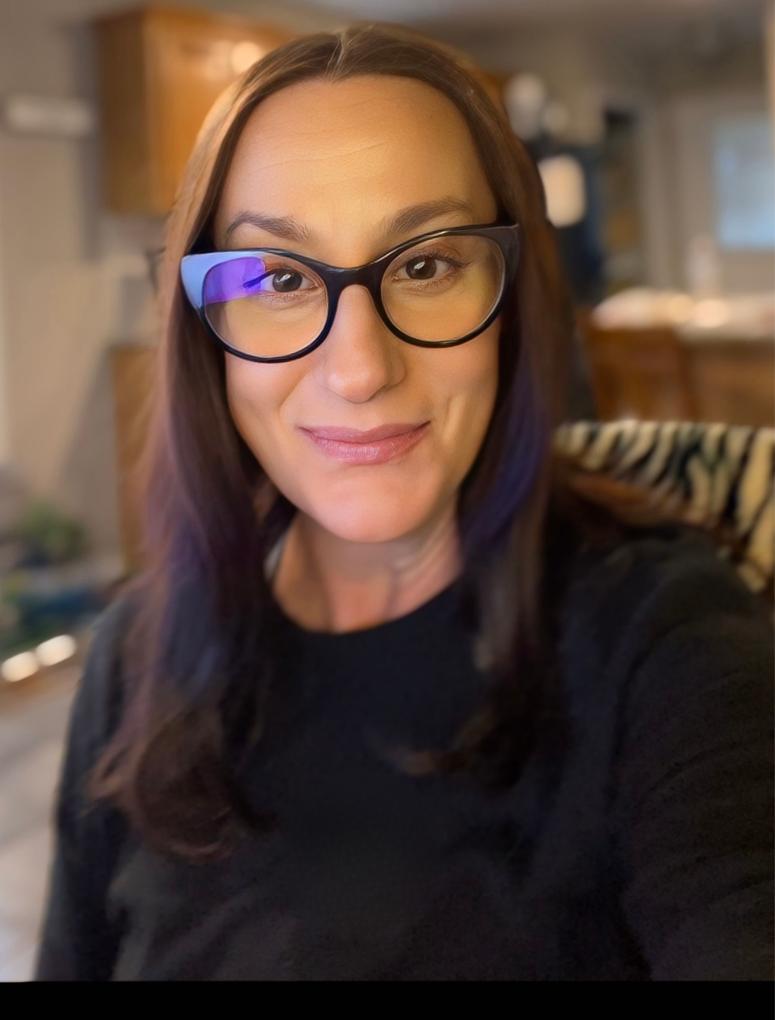 An honest woman with long, brown hair and glasses smiling indoors. Experienced diligence reasonable