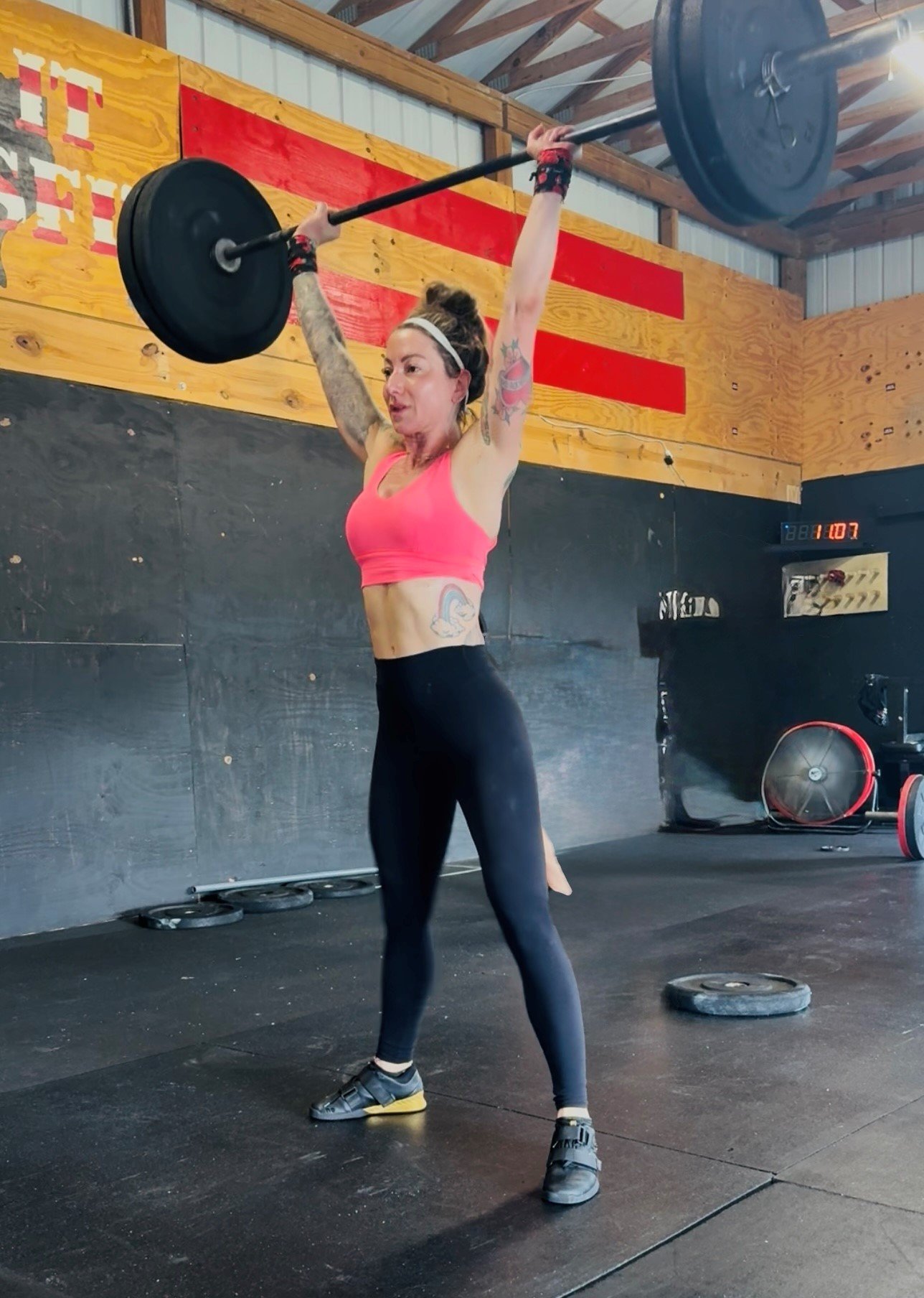 Woman in a gym lifting a loaded barbell overhead