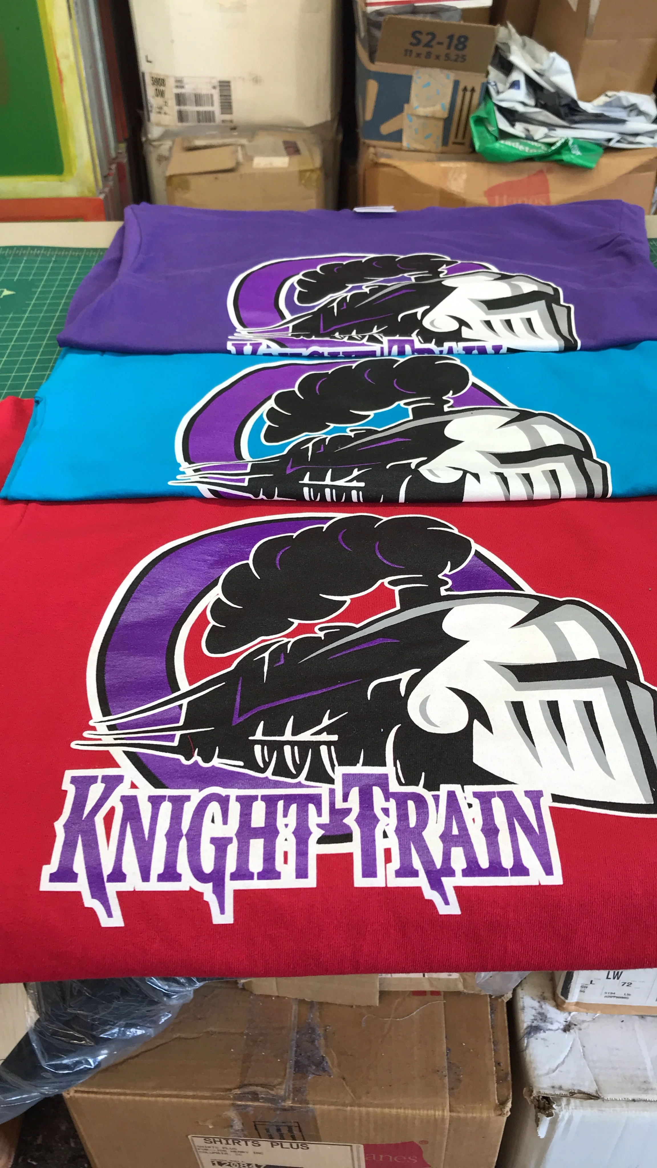Stacked custom screen printed t-shirts featuring a logo of a steam train with the words 'Knight Train' on each one.