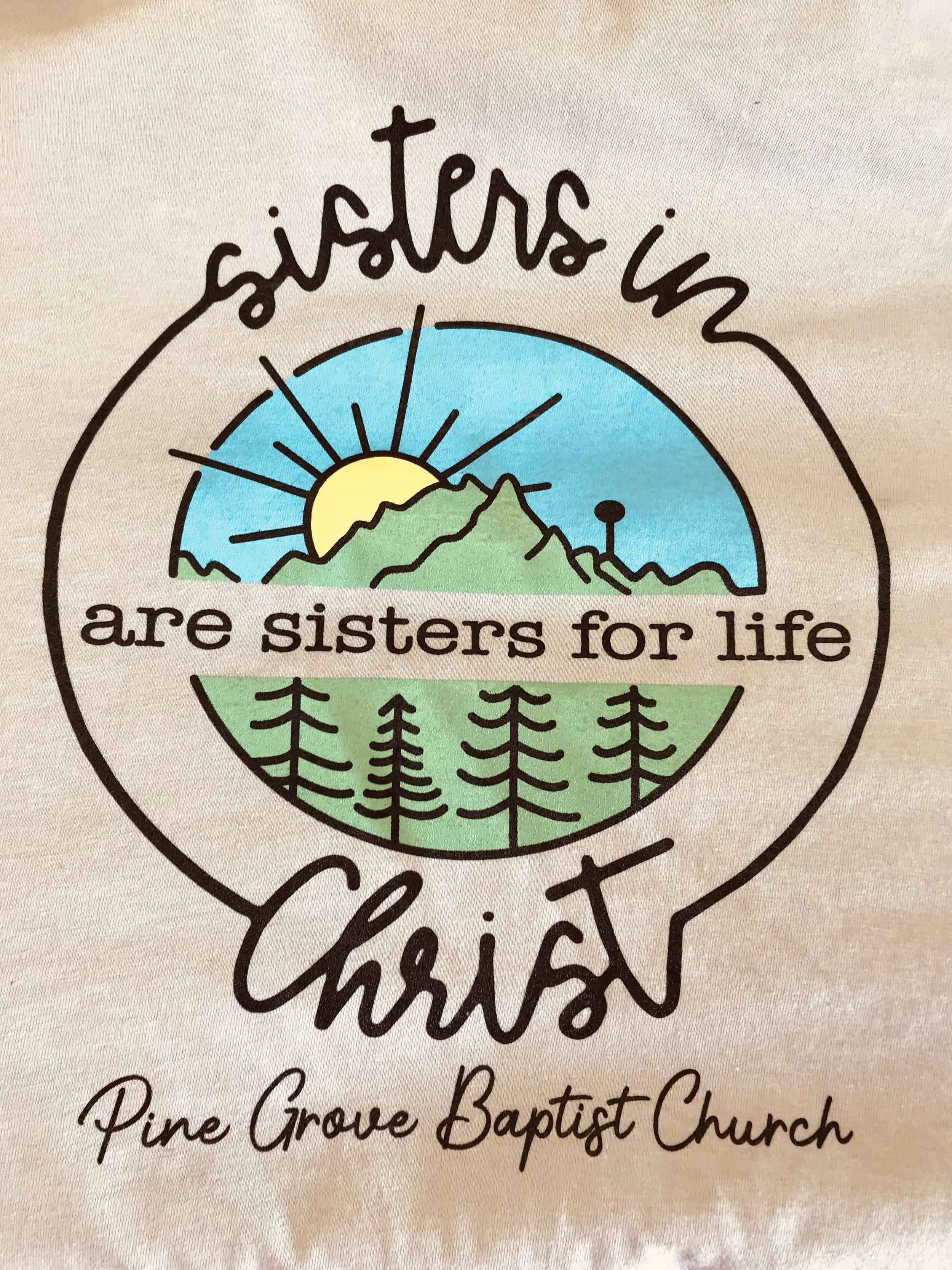 A circular logo featuring a sunrise over mountains and trees, with handwritten-style text around it, reading 'sisters in Christ' and 'are sisters for life'. Below, it says 'Pine Grove Baptist Church' Christian t-shirts custom church t-shirts