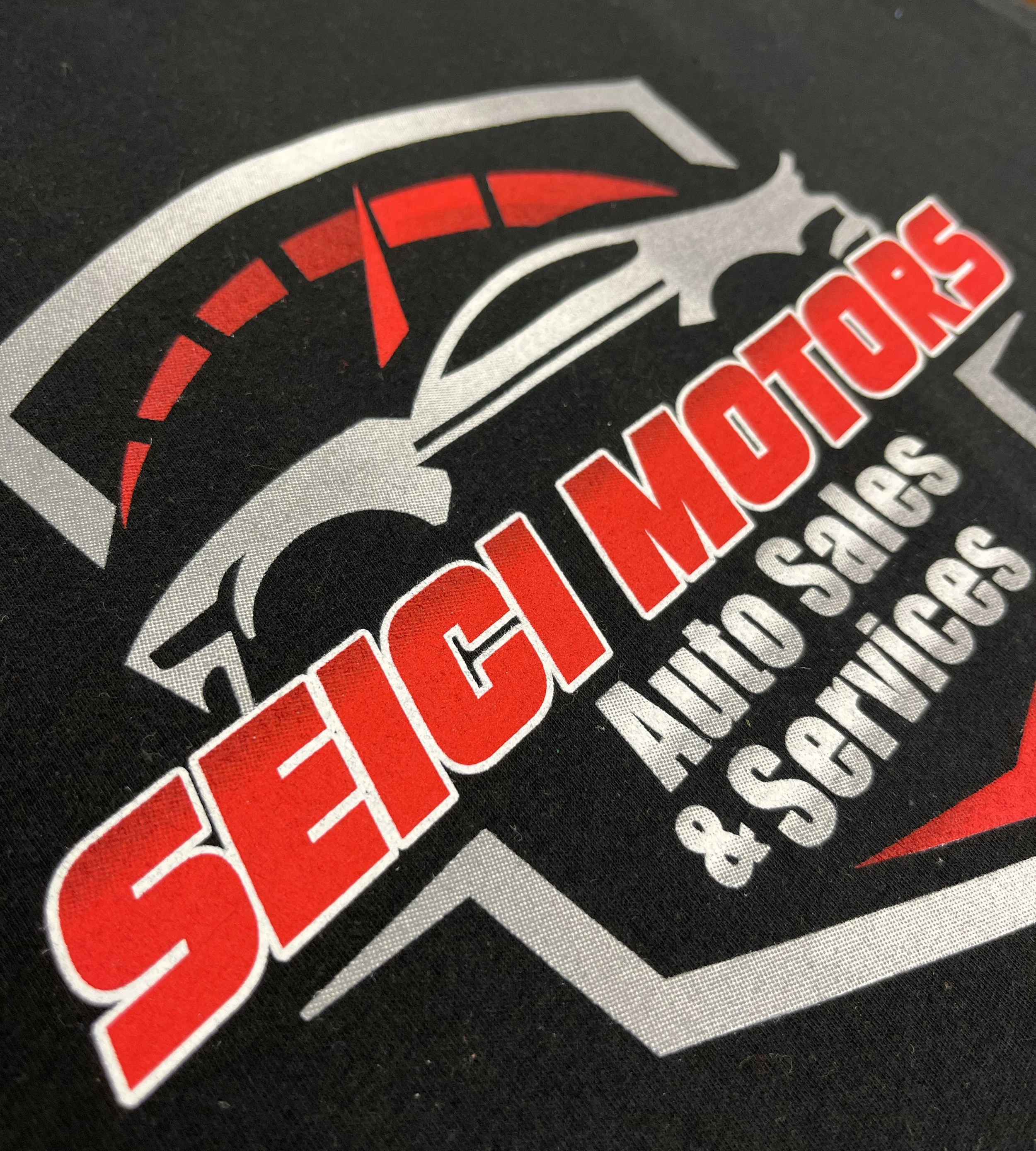 Close-up of a custom printed t-shirt featuring a stylized speedometer with a needle pointing to high speed, and the text 'seici motors' in bold red letters.