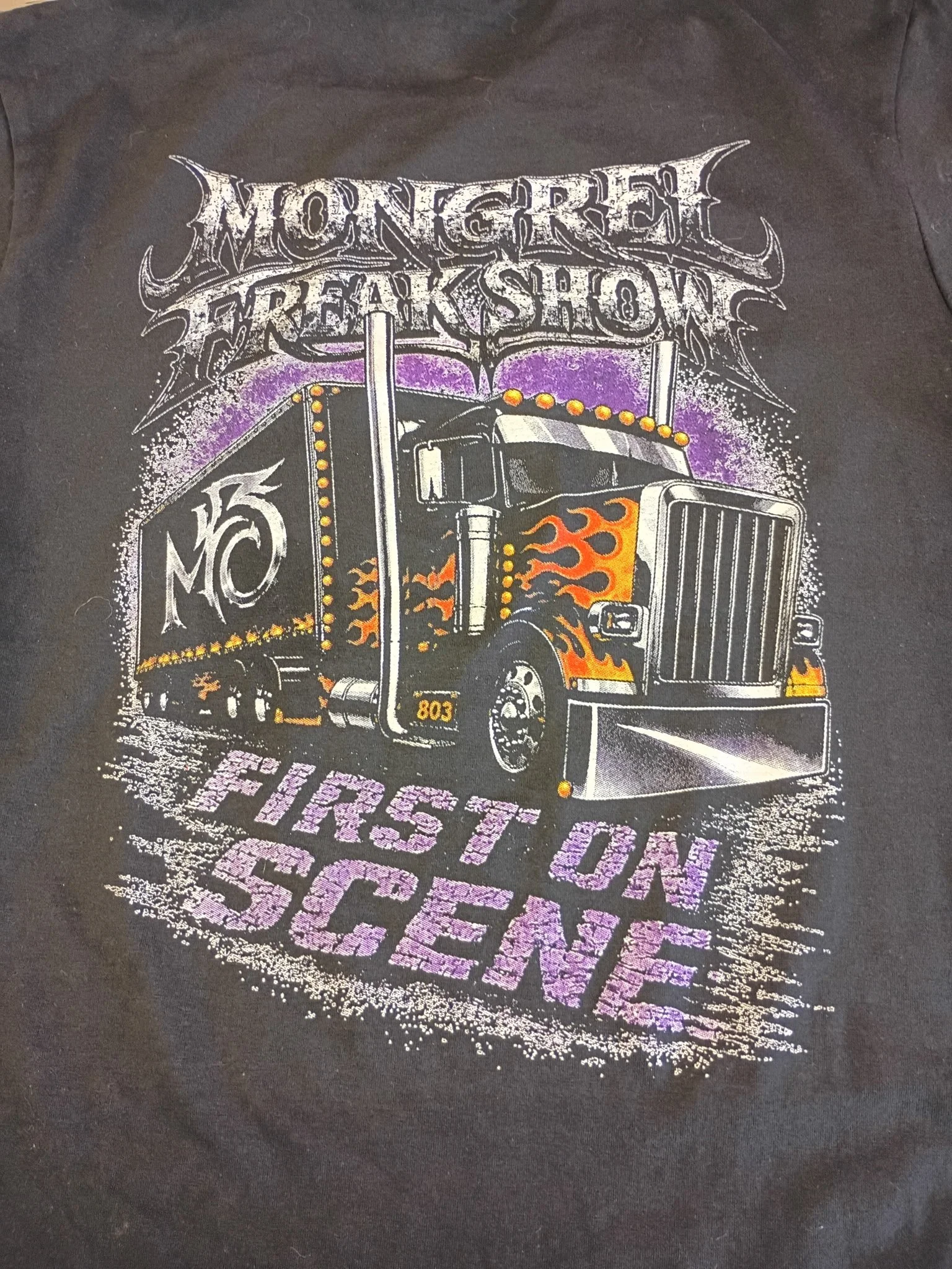 A black T-shirt featuring a colorful graphic design of a truck with flames, surrounded by stylized text reading 'the band name' and '803'.