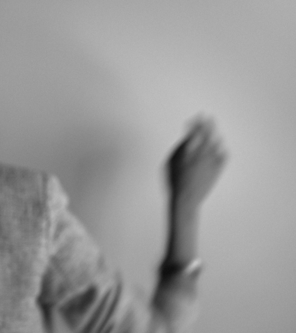 A blurred black and white photo of a person's hand with an open palm, reaching towards the sky, with a light-colored background.