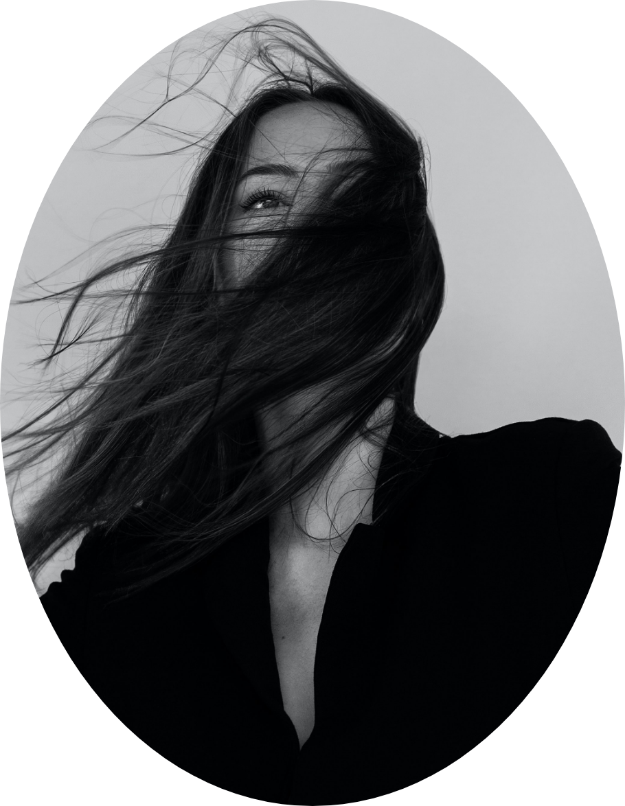 Black and white portrait of a woman with long hair covering her face, wearing a dark top, against a plain background.