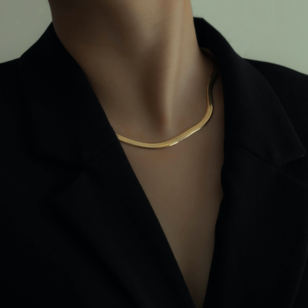 Close-up of a person wearing a gold necklace and a black blazer, with the focus on their neck and collar area.
