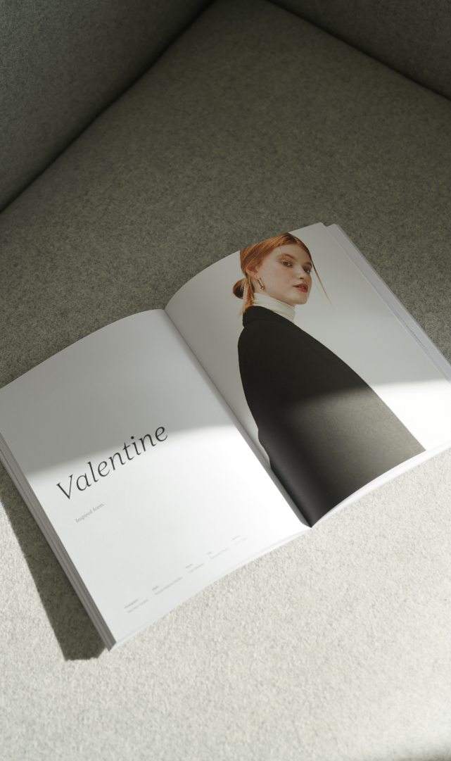 Open magazine on a light gray surface showing a woman in a black top on the right page and the word "Valentine" on the left page.