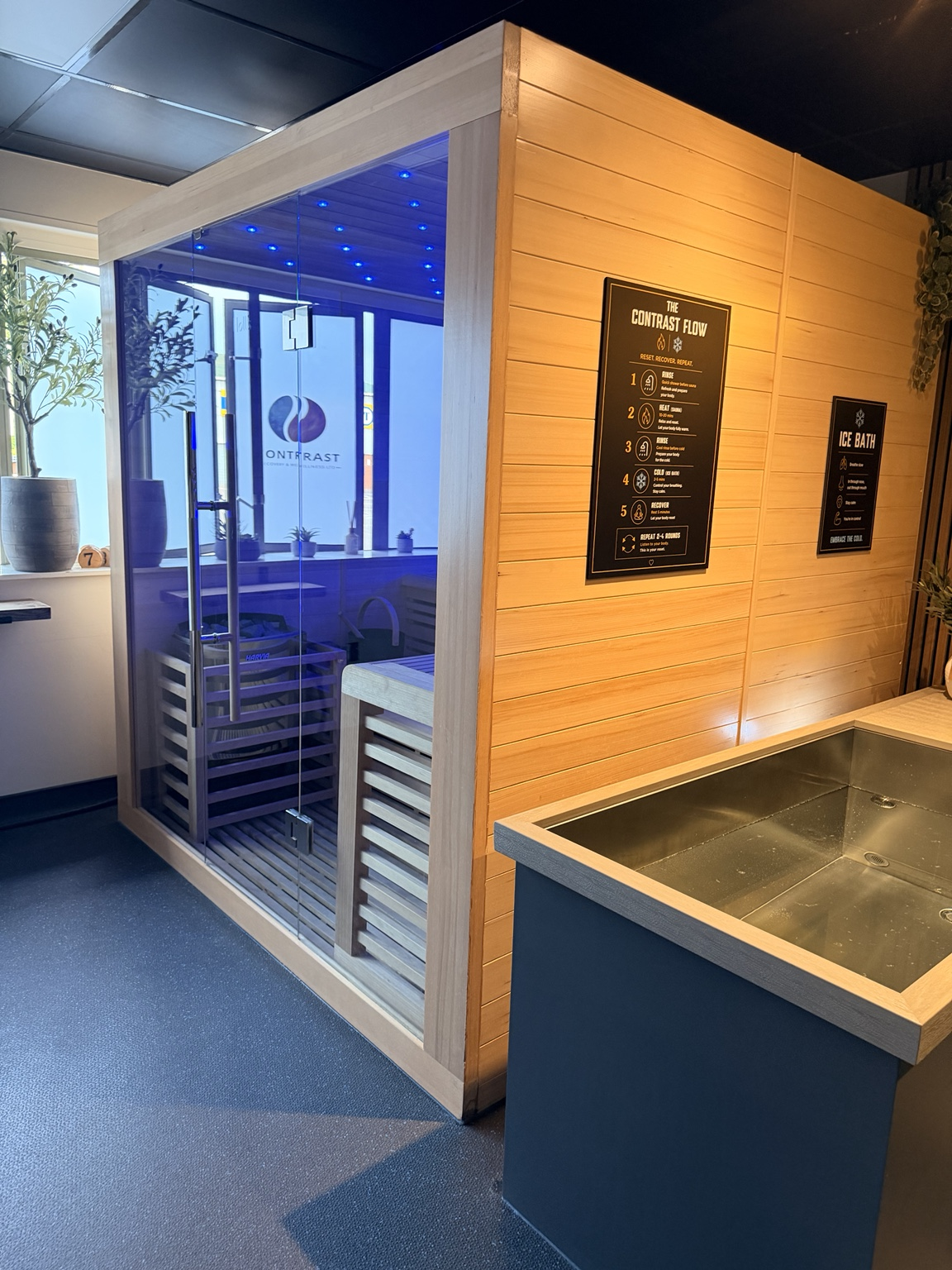 Traditional Finnish sauna  sauna with glass doors and wooden interior, next to a wooden panel with instructional posters, and premium Ice Baths.