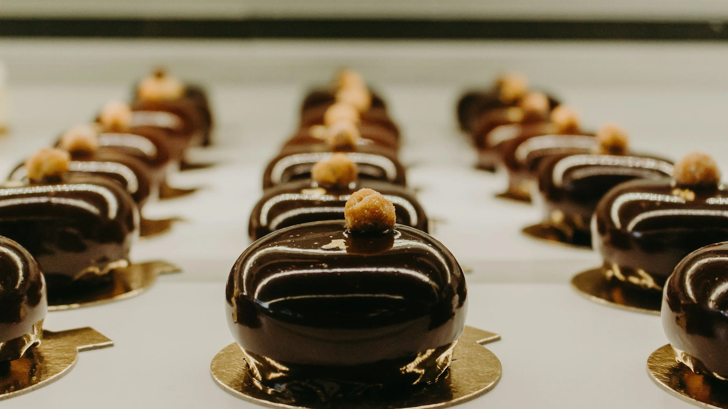 Close-up view of chocolate desserts topped with a small candy, arranged in rows on a tray.