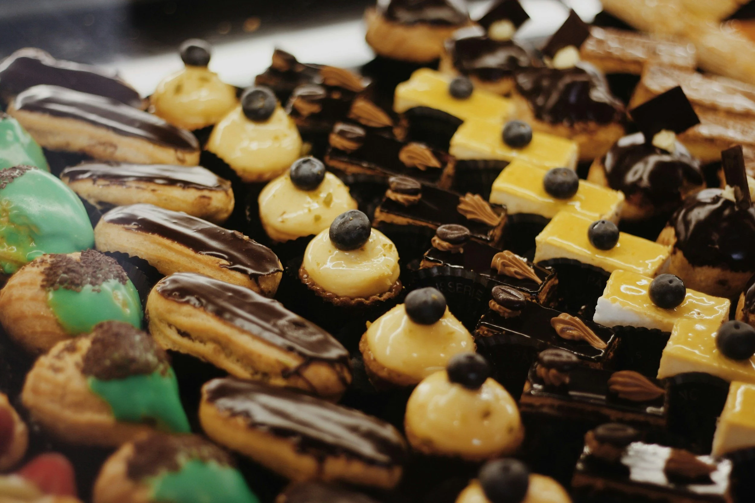 A variety of decorated pastries and petit fours, including cream-filled, chocolate-glazed, and fruit-topped varieties.