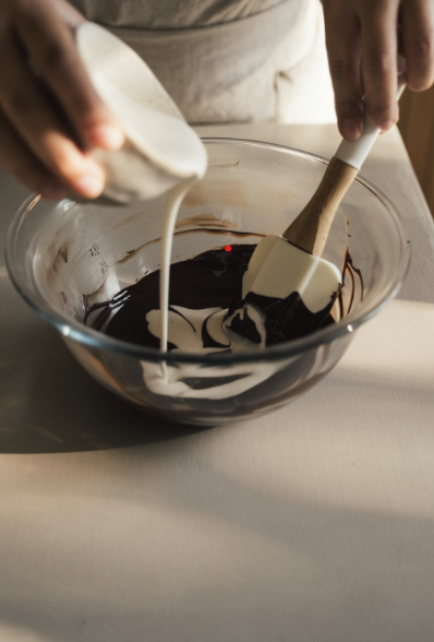 Pouring white cream into melted dark chocolate in a glass bowl.