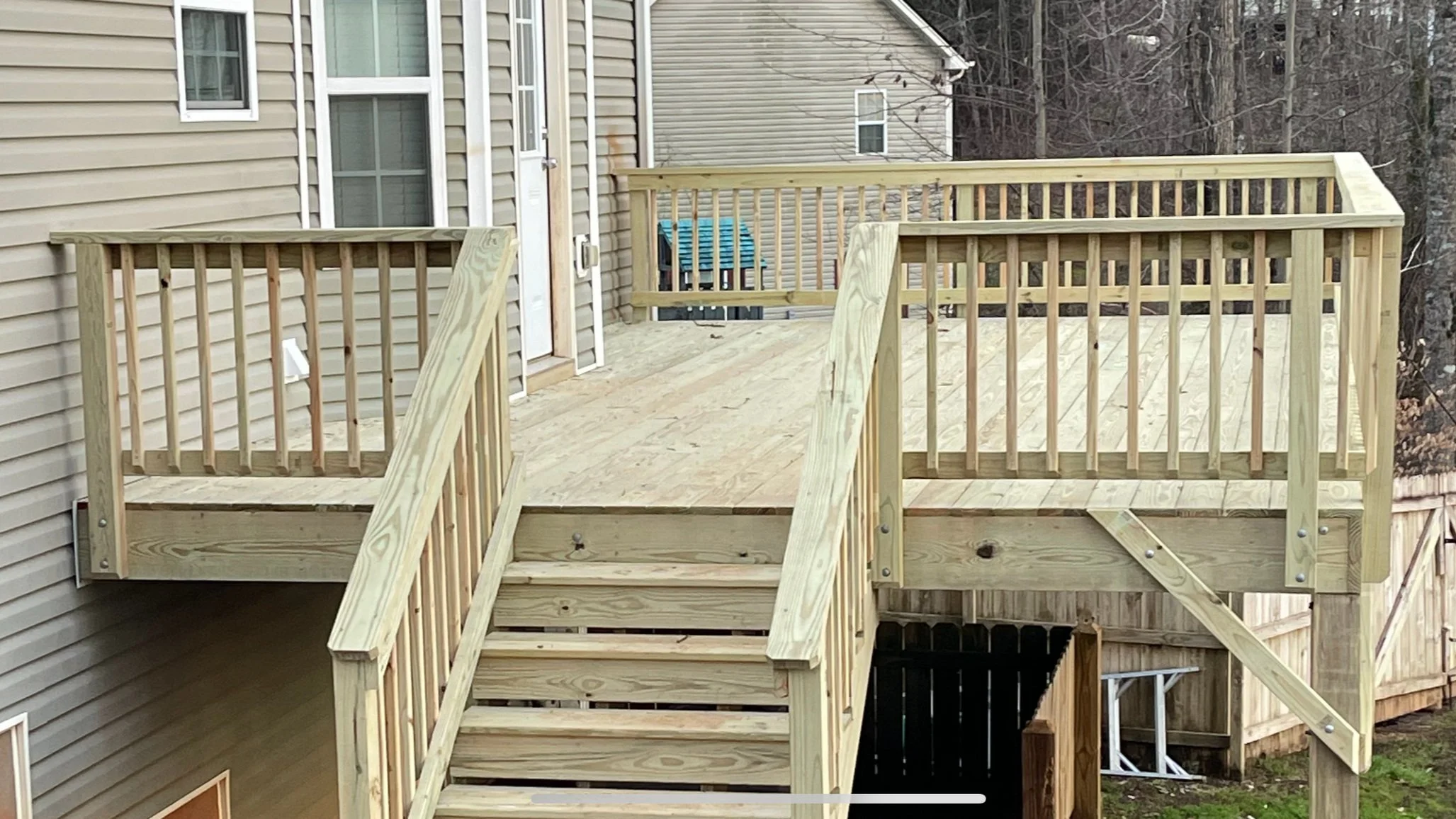 New wooden deck and stairs attached to a beige house with vinyl siding, overlooking a backyard with trees in the background.