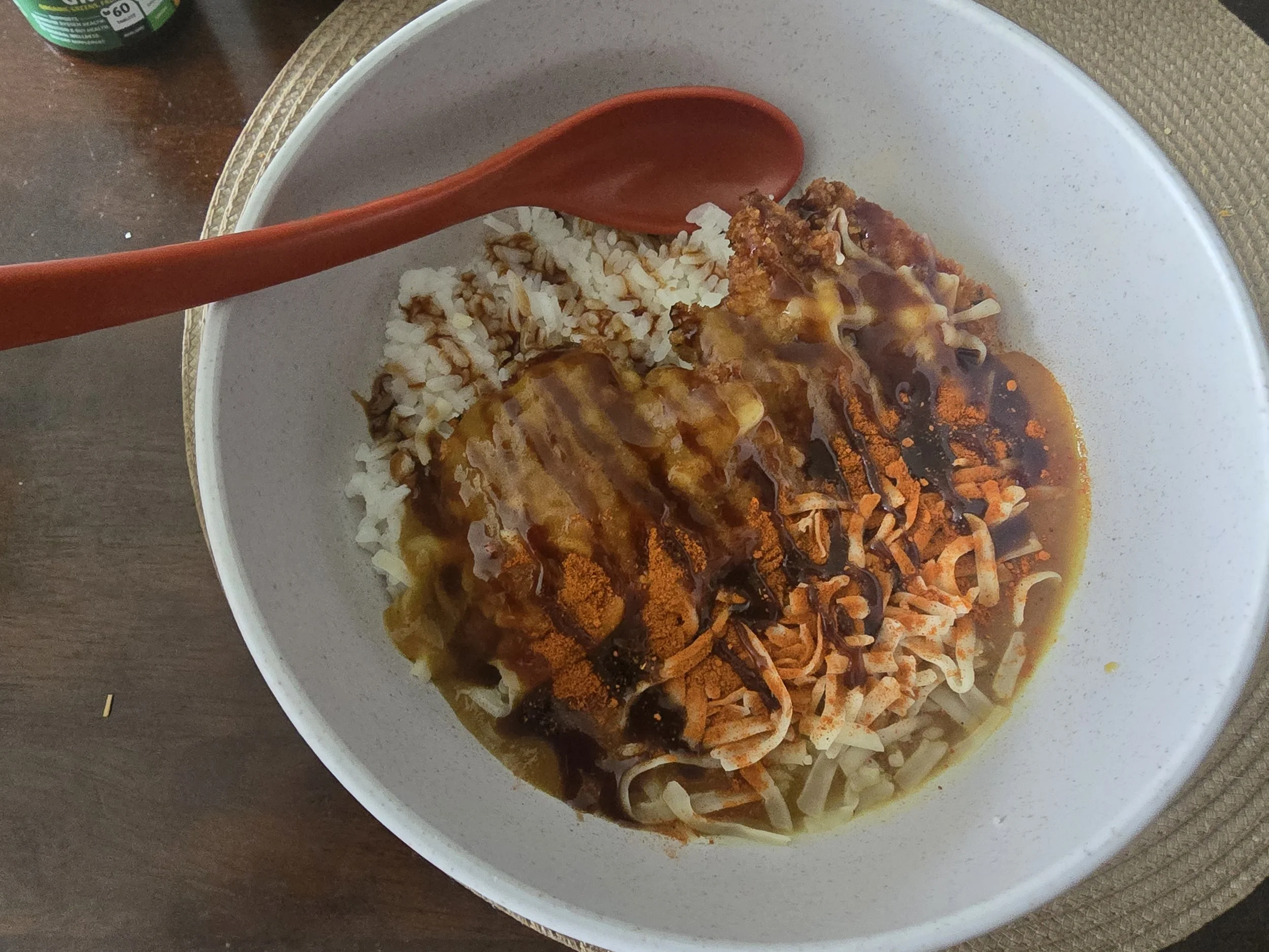 A white bowl with rice, shredded carrots, and fried chicken topped with gravy.