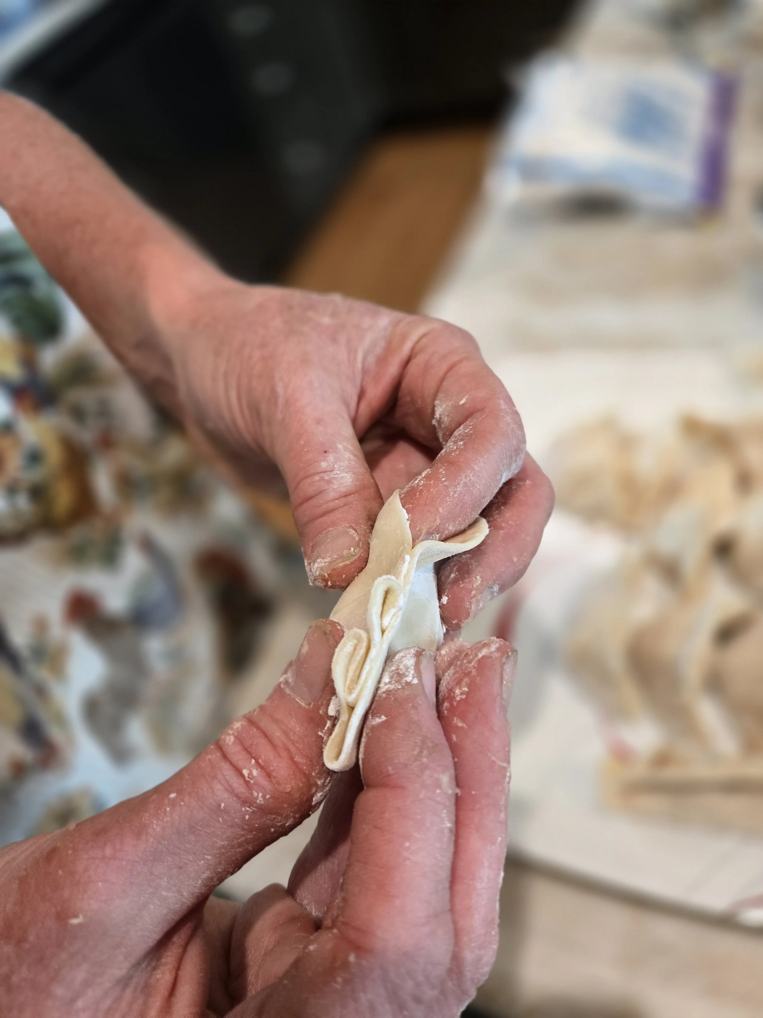 Close-up of hands shaping fresh pasta dough into a long strip in a kitchen setting.