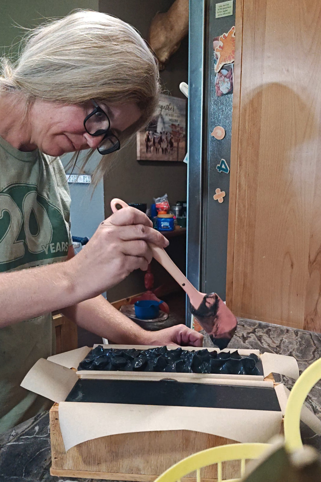 Woman using a spatula to create a design on the top of a loaf of goat milk soap