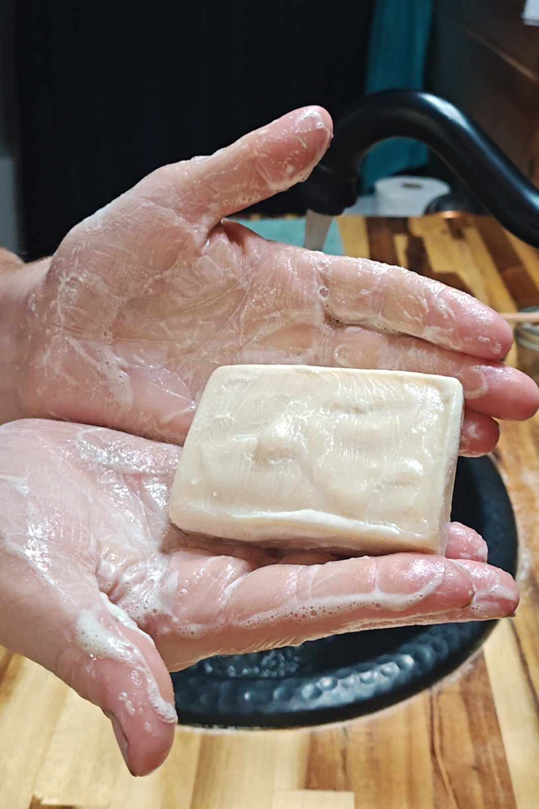 Hands lathered up from using goat milk soap, hold a bar in hand