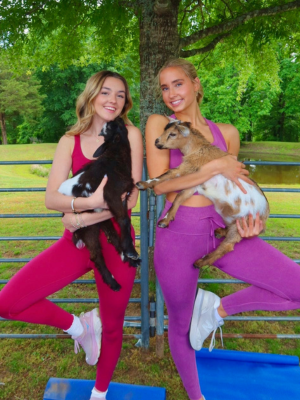 Two girls holding baby goats doing a yoga pose at a birthday party