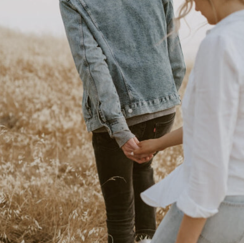A person kneeling and holding hands with another person in a field of dry grass.