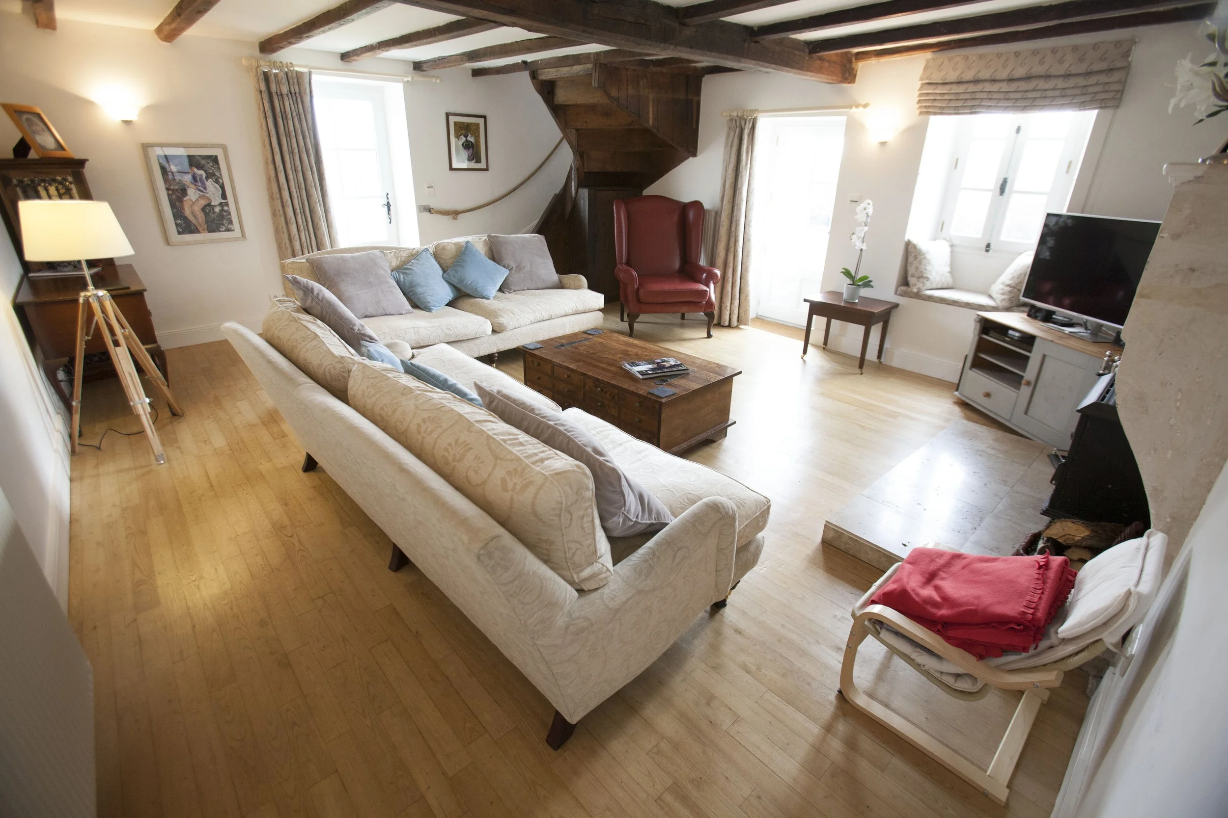 Living room with beige sofas, a wooden coffee table, red armchair, TV, and large windows with curtains.