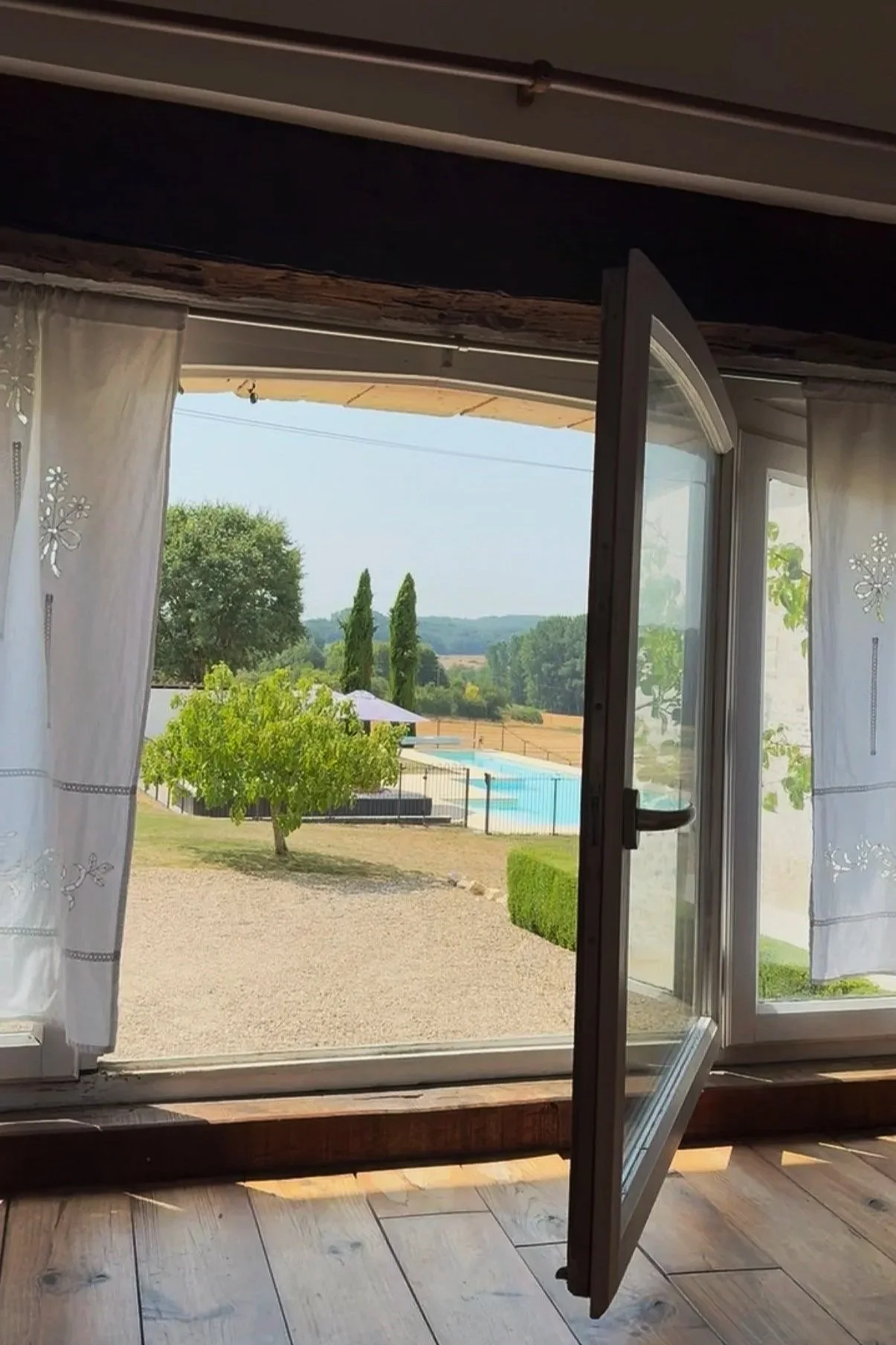 Open glass door leading to a backyard with a swimming pool, trees, and a landscape with rolling hills under a clear sky.