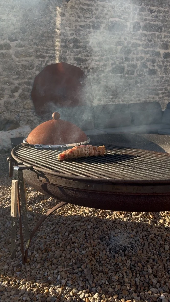 A grill outdoors with a lid and a sausage on the grill, next to a stone wall and a couch in the background.