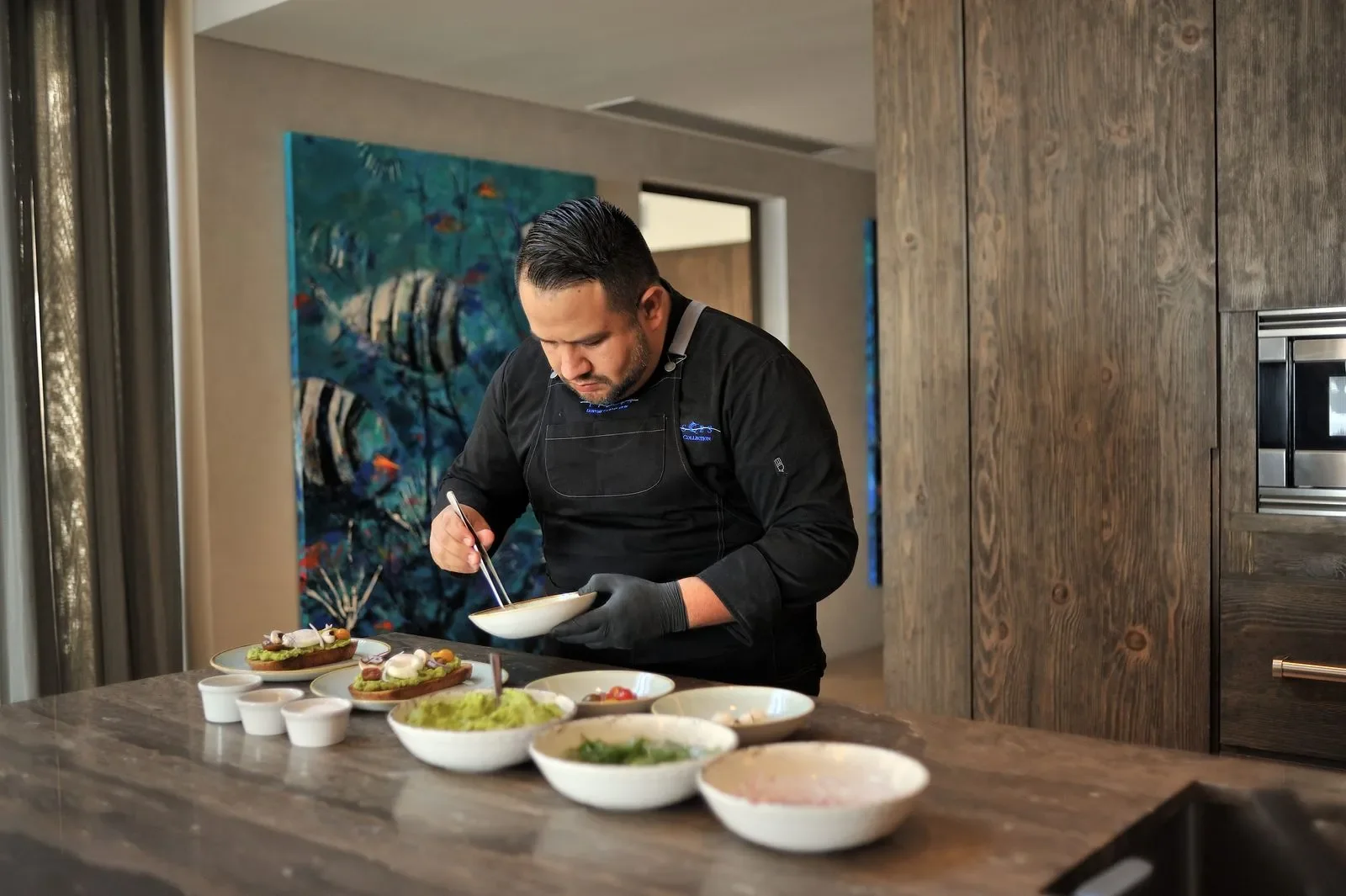 Chef preparing dishes in a modern kitchen with bowls of ingredients and plated food on a countertop.