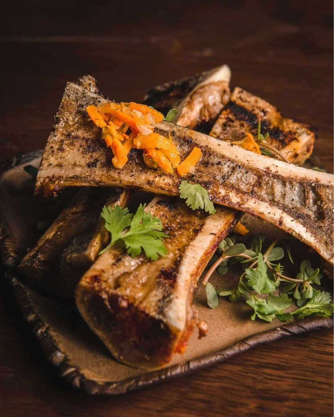 Grilled pork ribs garnished with fresh herbs and chopped vegetables on a decorative plate.