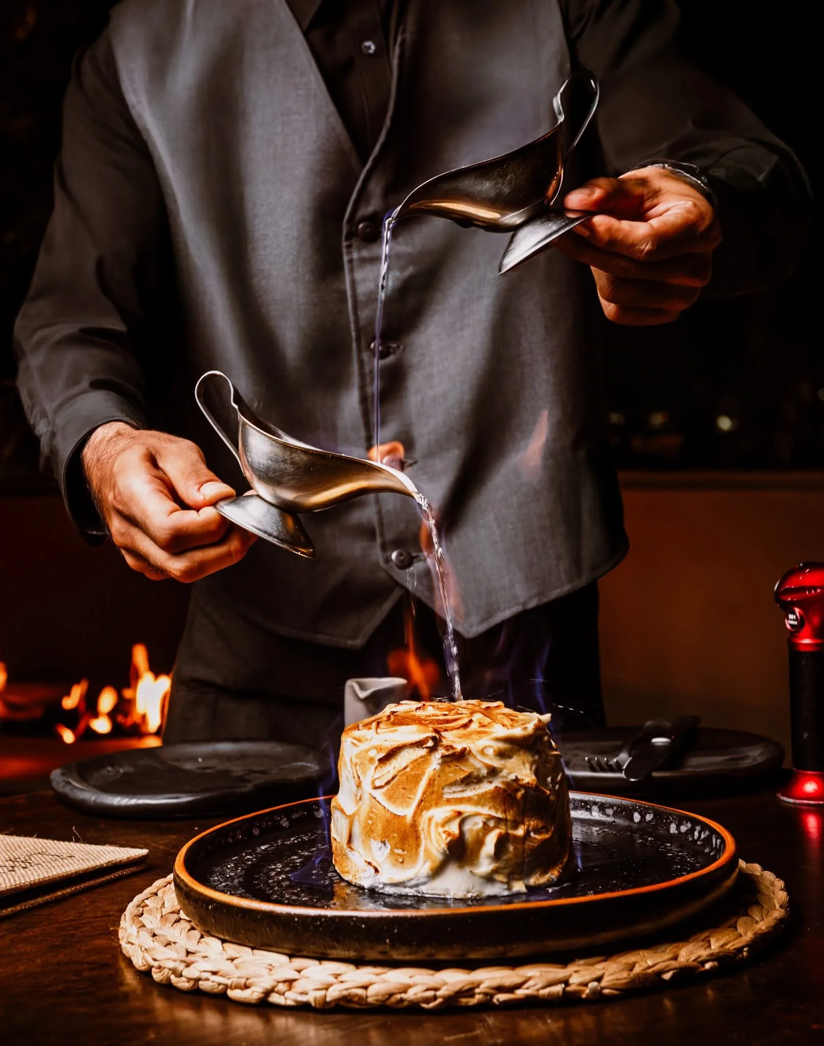 A person pouring caramel or syrup over a cake or dessert in a dark setting with a warm ambiance.