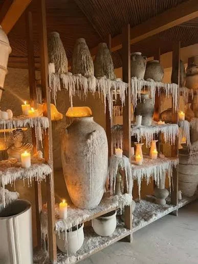 Shelving unit with large vases and candles, decorated with artificial snow and icicles for winter or holiday decor.