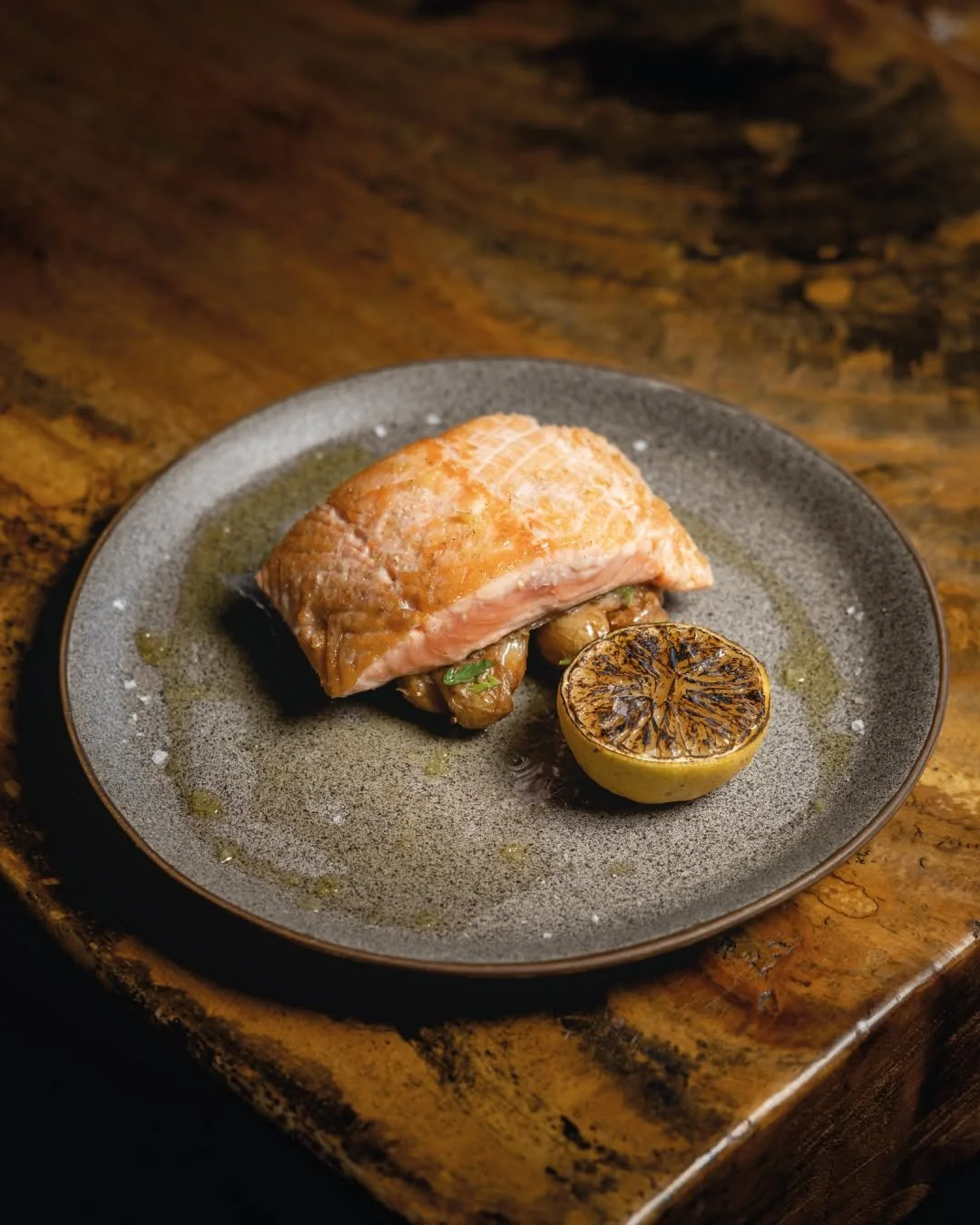A plate of cooked salmon fillet served with grilled lemon plated on a rustic wooden table.