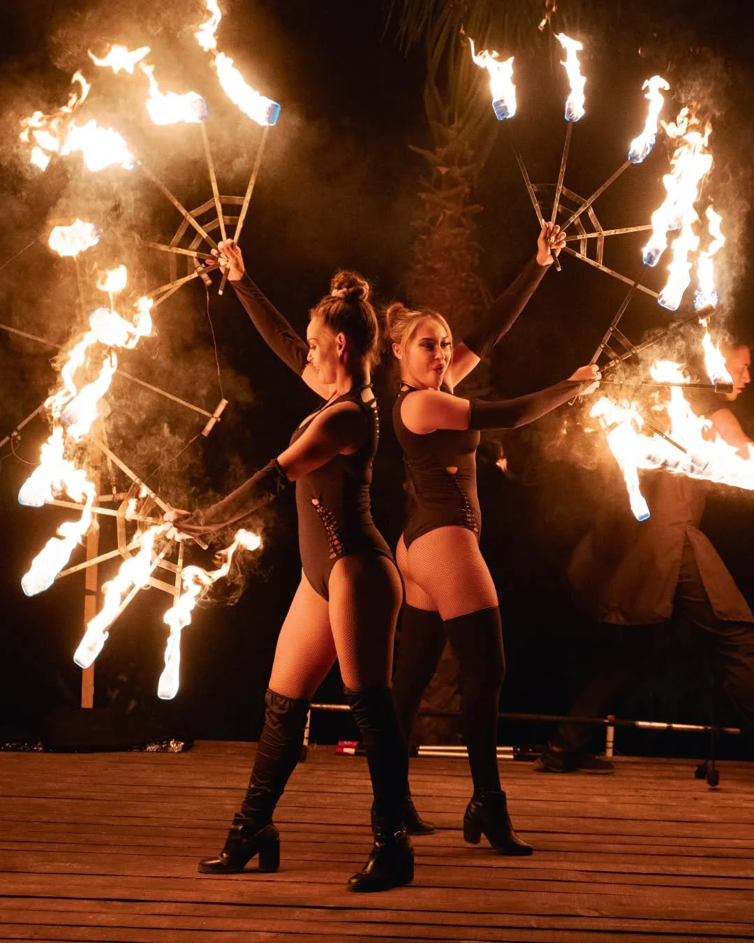 Two women perform a fire dance on a wooden stage at night, holding fire wands with flames.