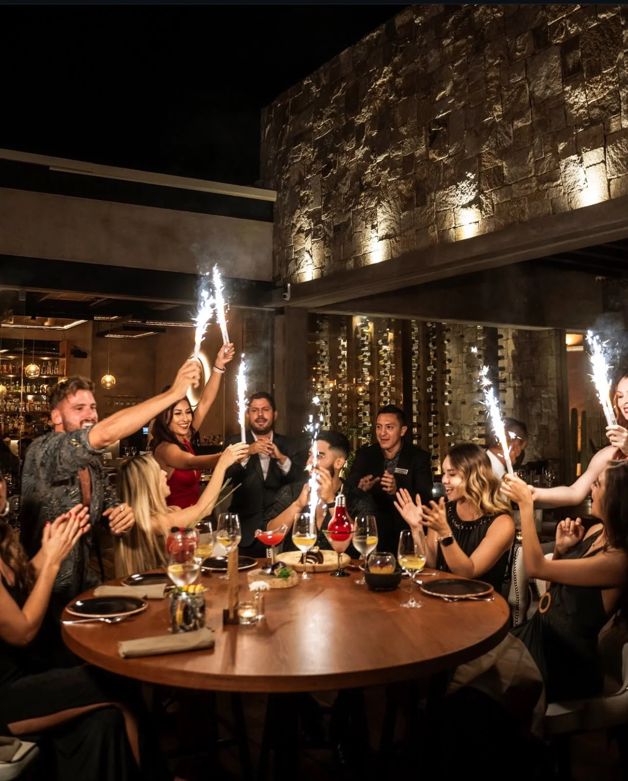 Group of friends celebrating at a dinner party with sparklers in a restaurant, with smiling faces and festive atmosphere.