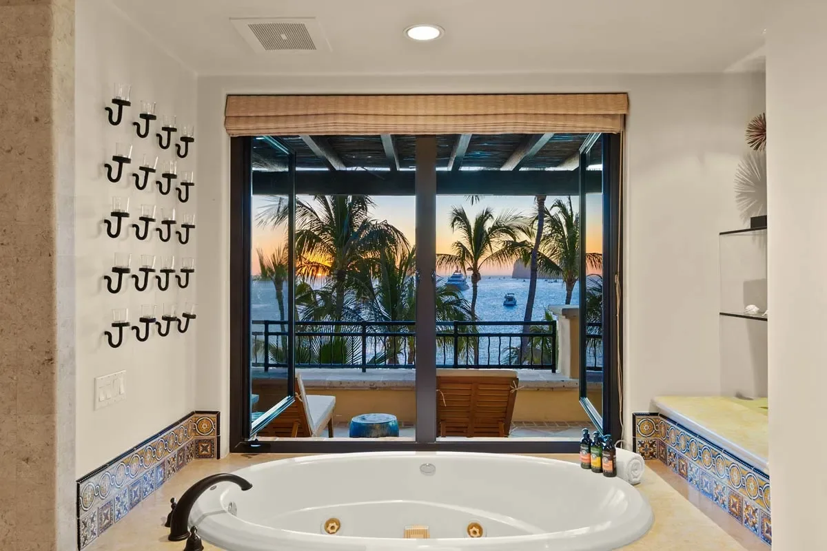 Bathroom with a jacuzzi tub overlooking a balcony with view of palm trees, ocean, and sunset