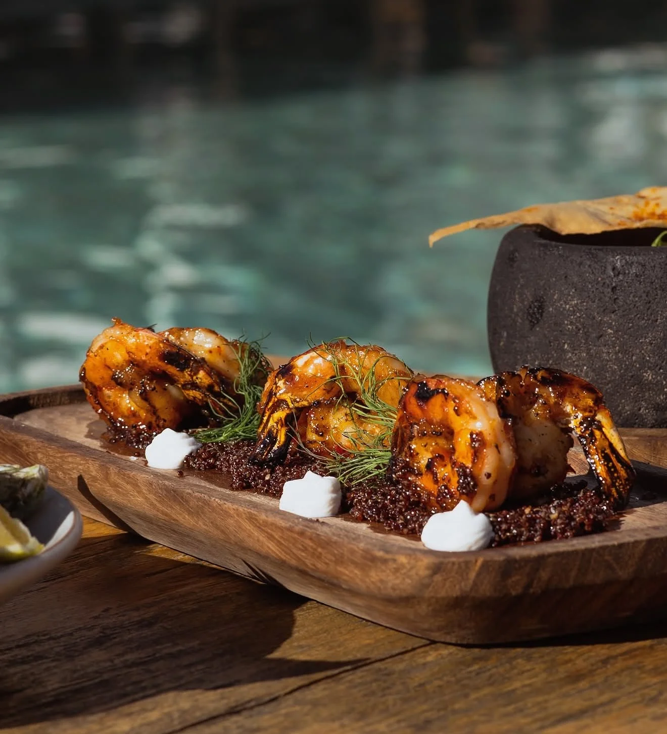 Grilled shrimp garnished with herbs and served on a bed of sauce, with a backdrop of water.