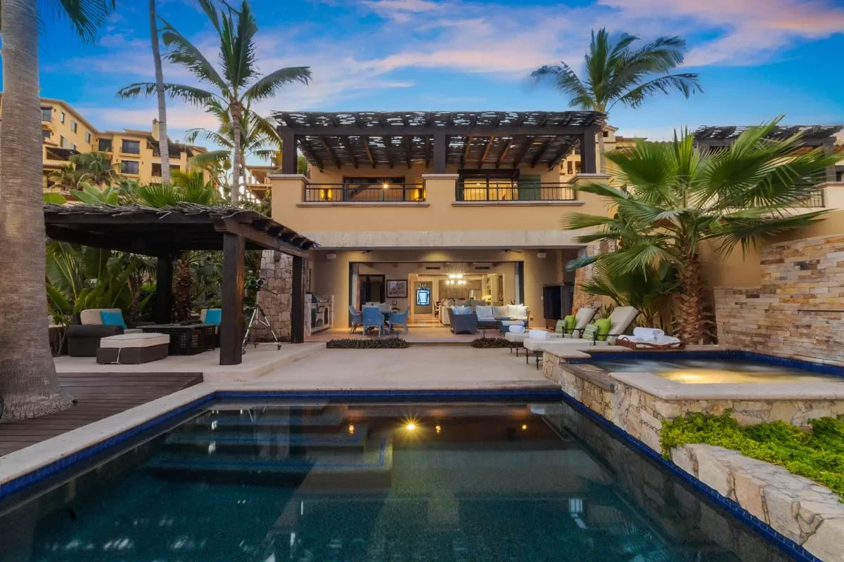 Luxury backyard with a swimming pool, palm trees, and outdoor seating area, sunset sky in the background.