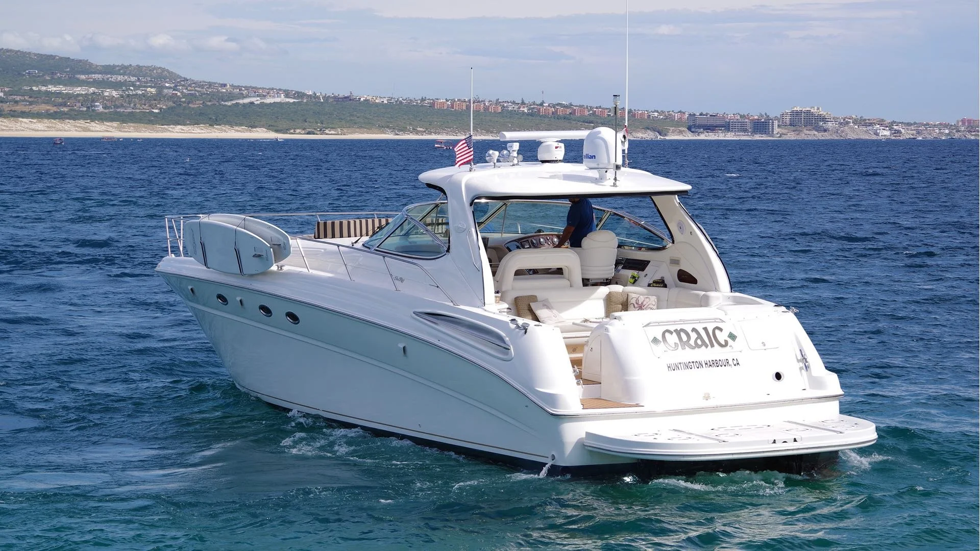 White yacht sailing on blue water with a scenic coastline in the background, displaying the name 'CRAIG' and 'Huntington Harbour, CA'.