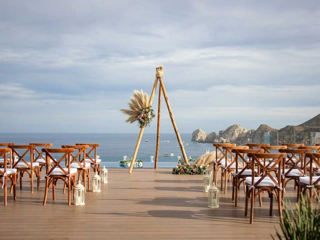 Outdoor wedding setup overlooking the ocean with wooden chairs, a decorated arch, and scenic coastal cliffs in the background.