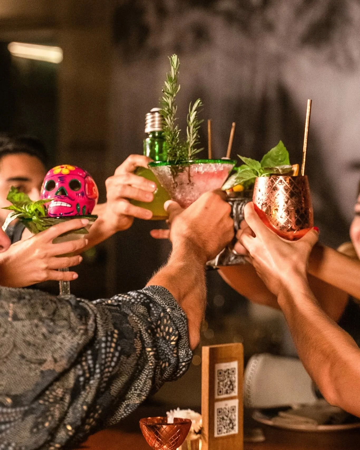 People raising colorful cocktails in a toast at a bar or restaurant.