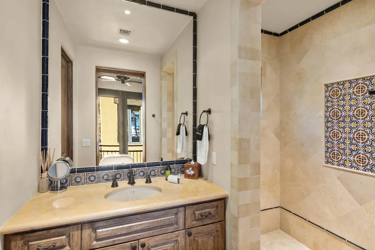 Bathroom with a beige vanity, large mirror, and a walk-in shower with decorative tile accents.