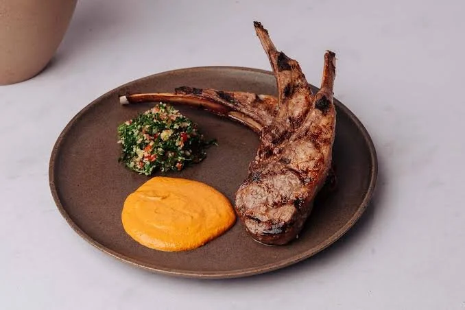 Grilled lamb chop with herb sauce and mashed sweet potatoes on a brown plate.
