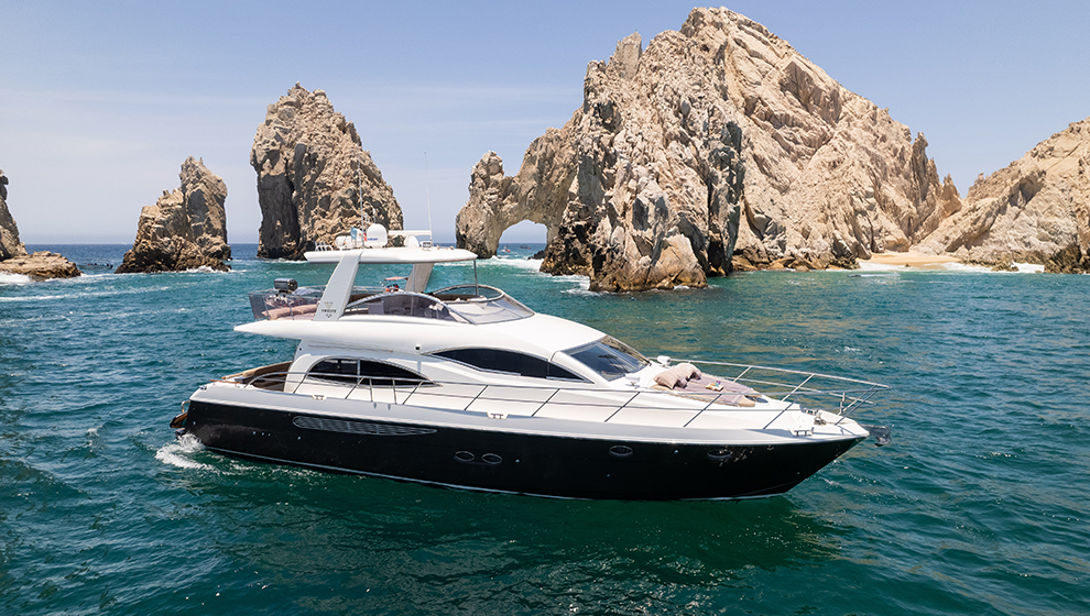 Luxury yacht sailing near rocky island formations in blue water, under a clear sky.