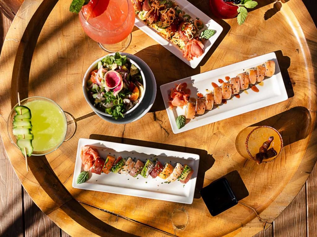 Sushi, salads, and cocktails on a round wooden table.