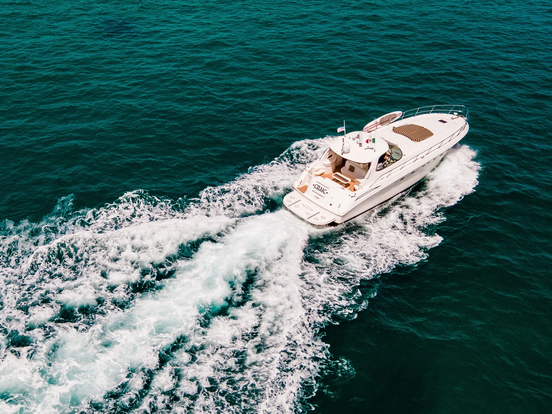 A white yacht moving at high speed on the open ocean, creating a wake behind it with blue-green water.