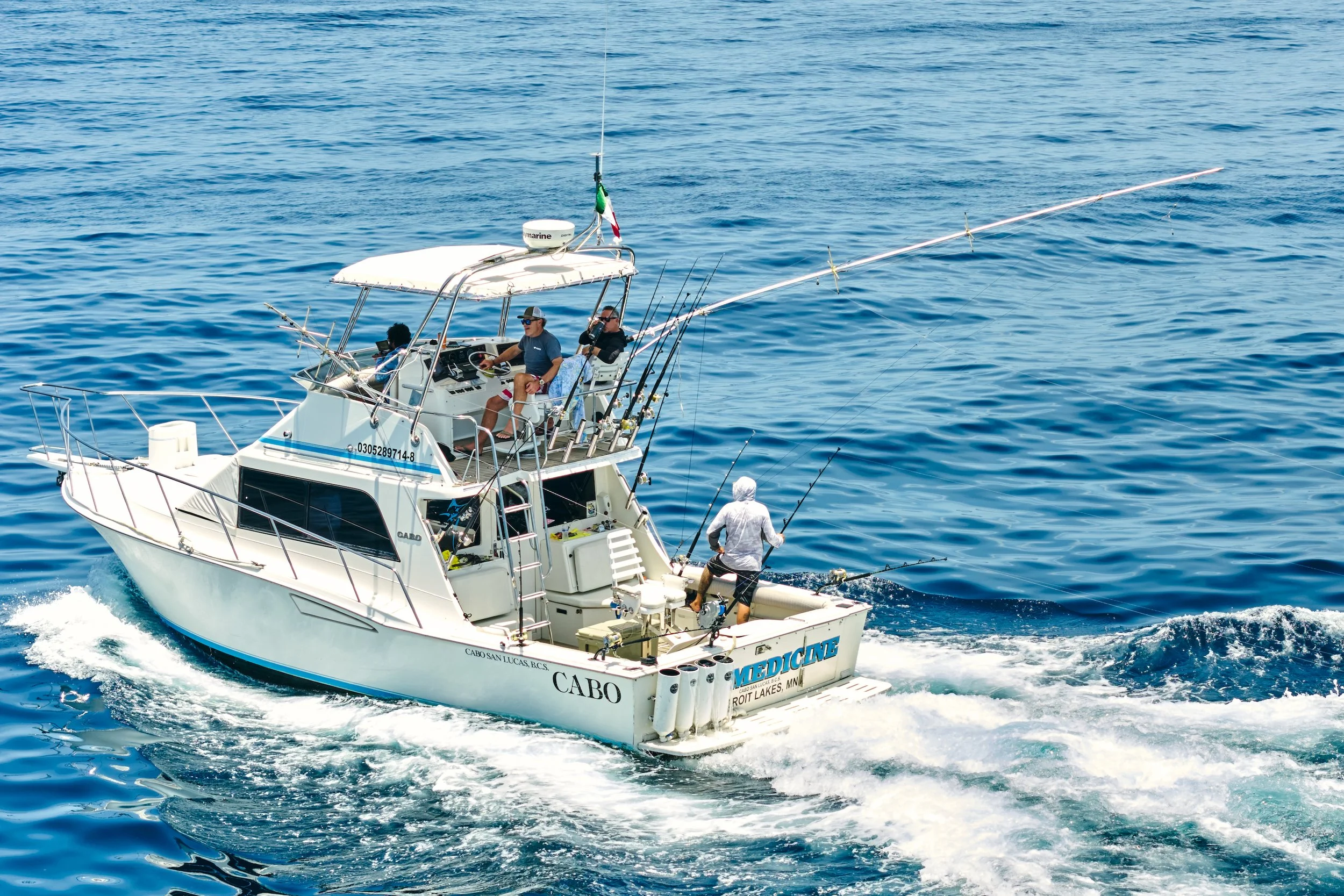 A white fishing boat with multiple anglers fishing in calm blue ocean water.