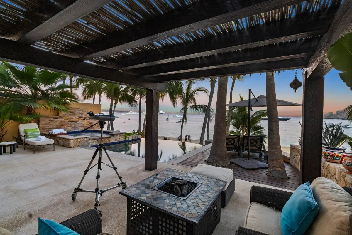 Beachside patio with seating area, telescope, palm trees, pool, and ocean view at sunset