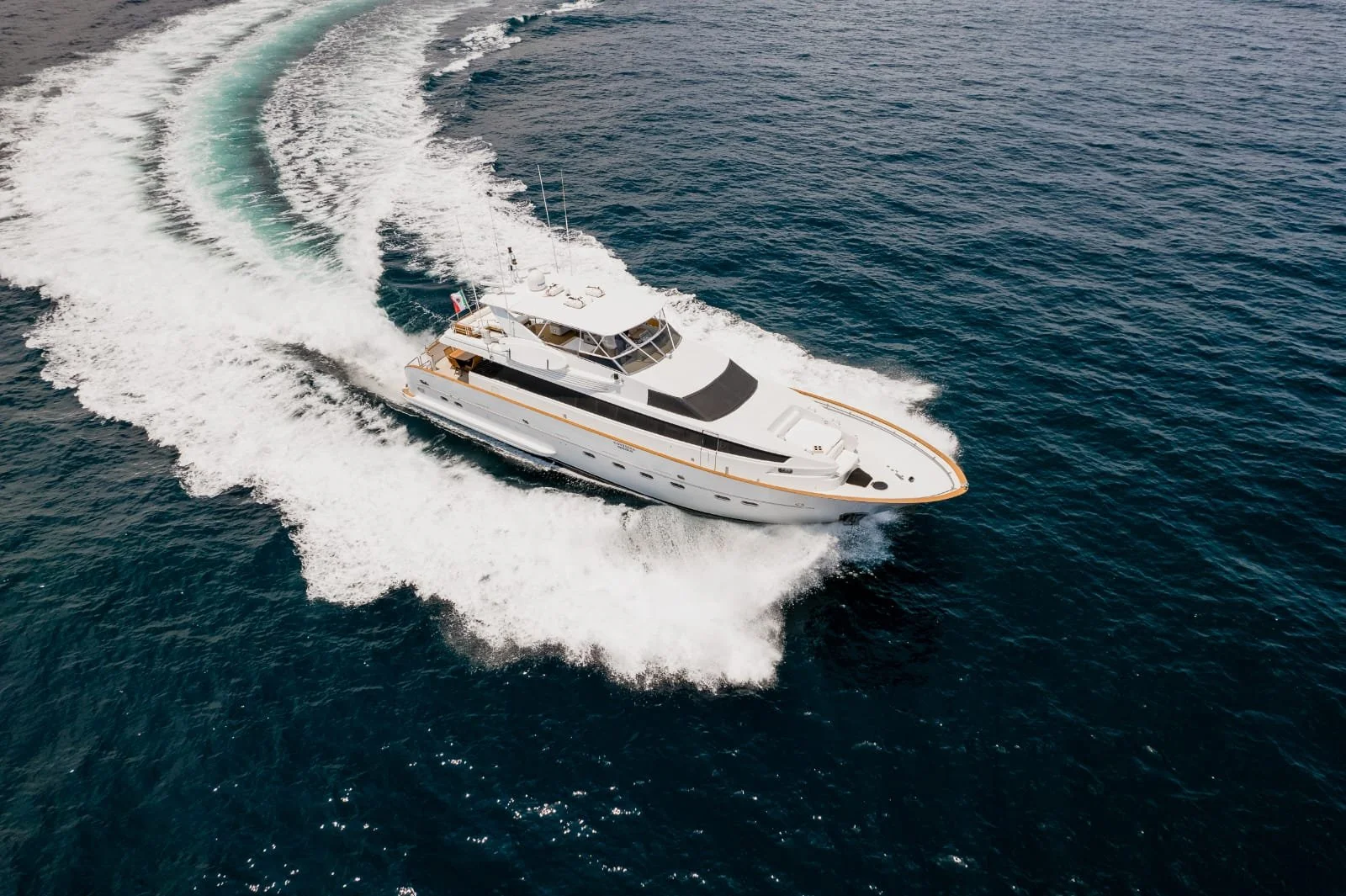 A white luxury yacht sailing through the ocean, creating a wake behind it.