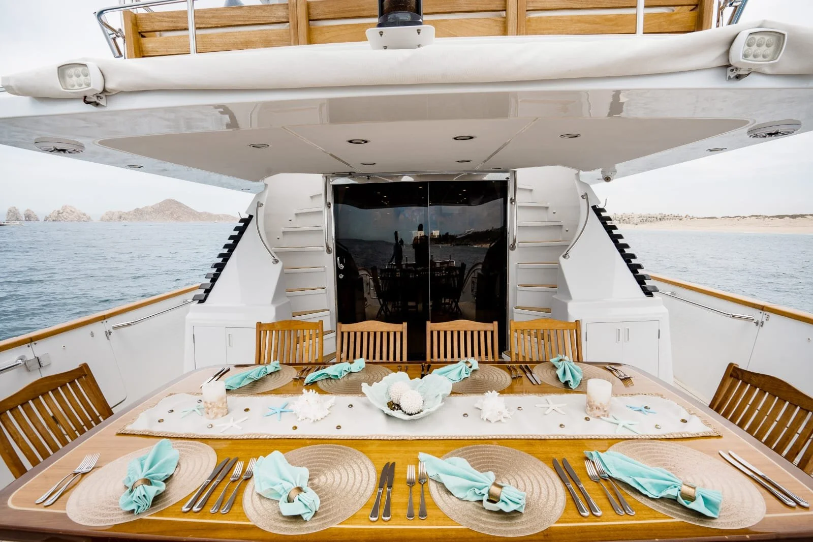A dining table set for a meal on a yacht with ocean and distant islands in the background.